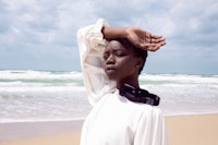 a black woman standing on the beach with her hand on her head