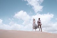 two women standing on top of a sand dune