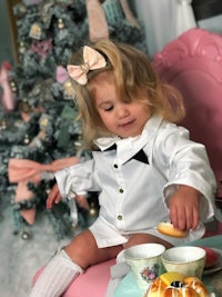 a little girl sitting on a pink chair with a cup of tea