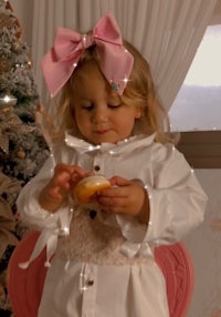 a little girl eating an orange in front of a christmas tree