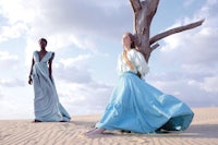 two women in blue dresses standing in the sand