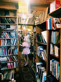 a girl in a pink dress walking through a book store