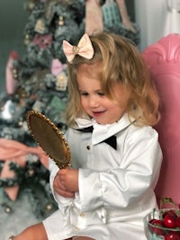 a little girl holding a mirror in front of a christmas tree