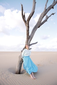 a woman in a blue dress leaning against a dead tree