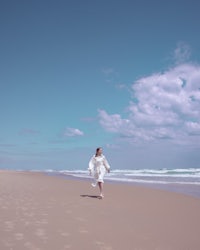 a woman in a white dress running on the beach